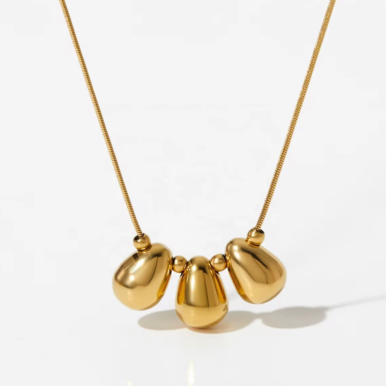 Trio d’Or Halskette mit drei goldenen, glatten Kugel- und Tropfenformen an goldener Kette.
