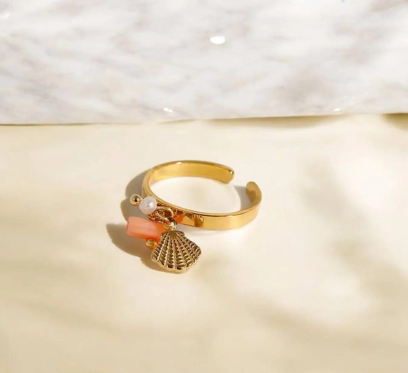 Eleganter goldener Ring Glossy Shell mit Muschel-Anhänger, Perle und Korallen-Detail. Perfektes Schmuckstück für stilvolle Looks.