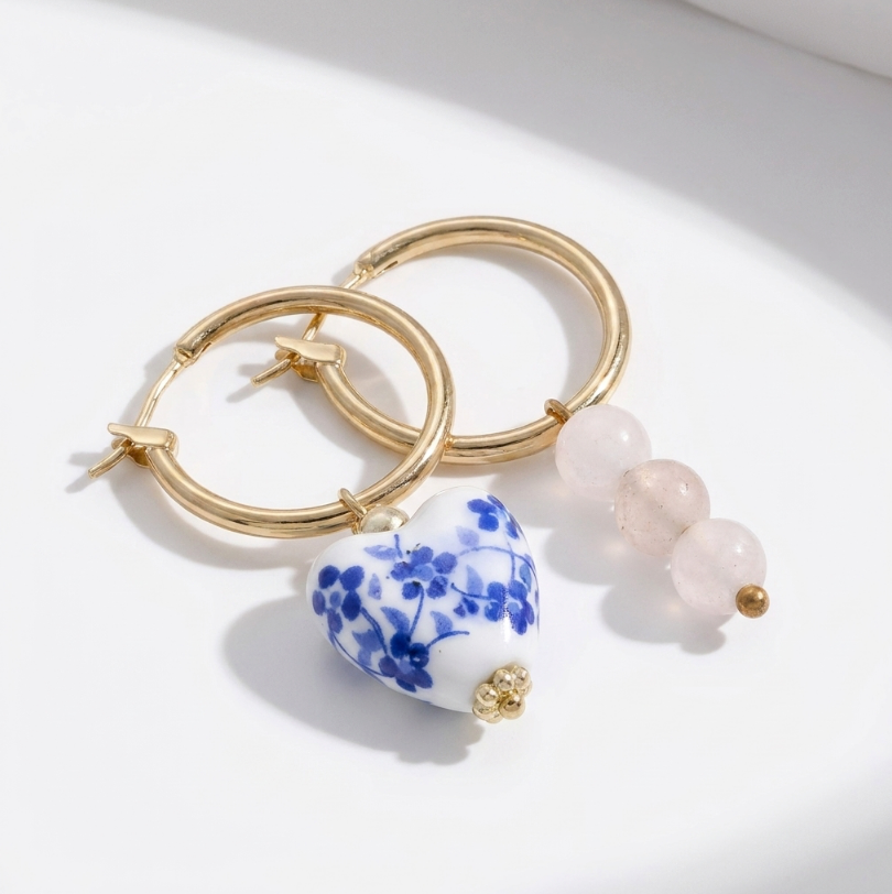Blue Belle Ohrringe: Goldene Creolen mit blau-weißem Keramikherz mit Blütenmuster und rosa Perlenanhänger.