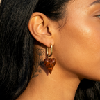 Safari Heart Ohrring: goldener Haken mit braun marmoriertem Herzanhänger am Ohr, sichtbare Hals-Tätowierung.